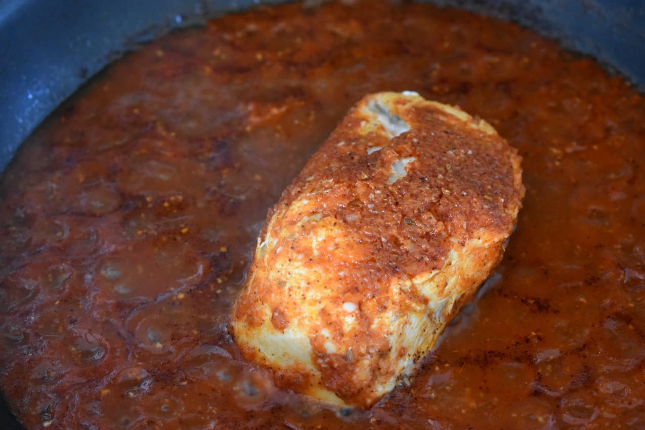 A chicken breast cooking in enchilada sauce.
