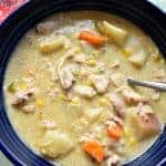 A blue bowl filled with slow cooker chicken and corn chowder and a spoon.