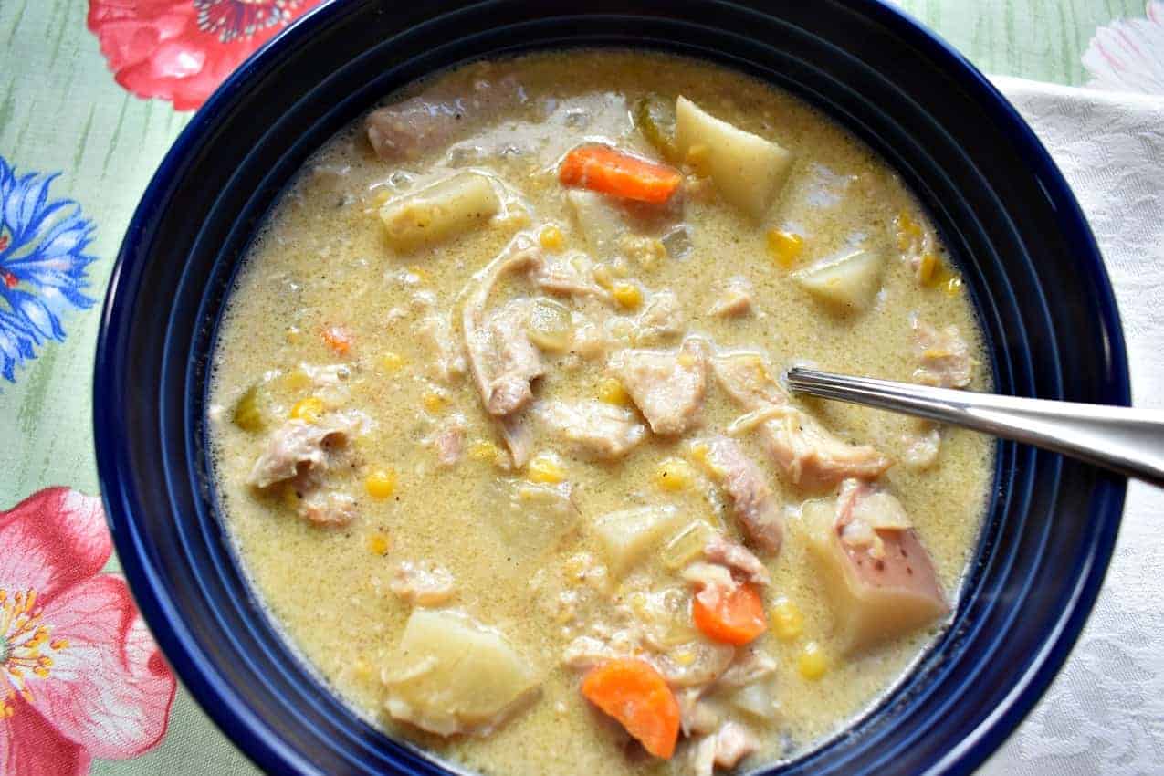 Overhead view of a blue bowl filled with slow cooker chicken and corn chowder and a spoon.