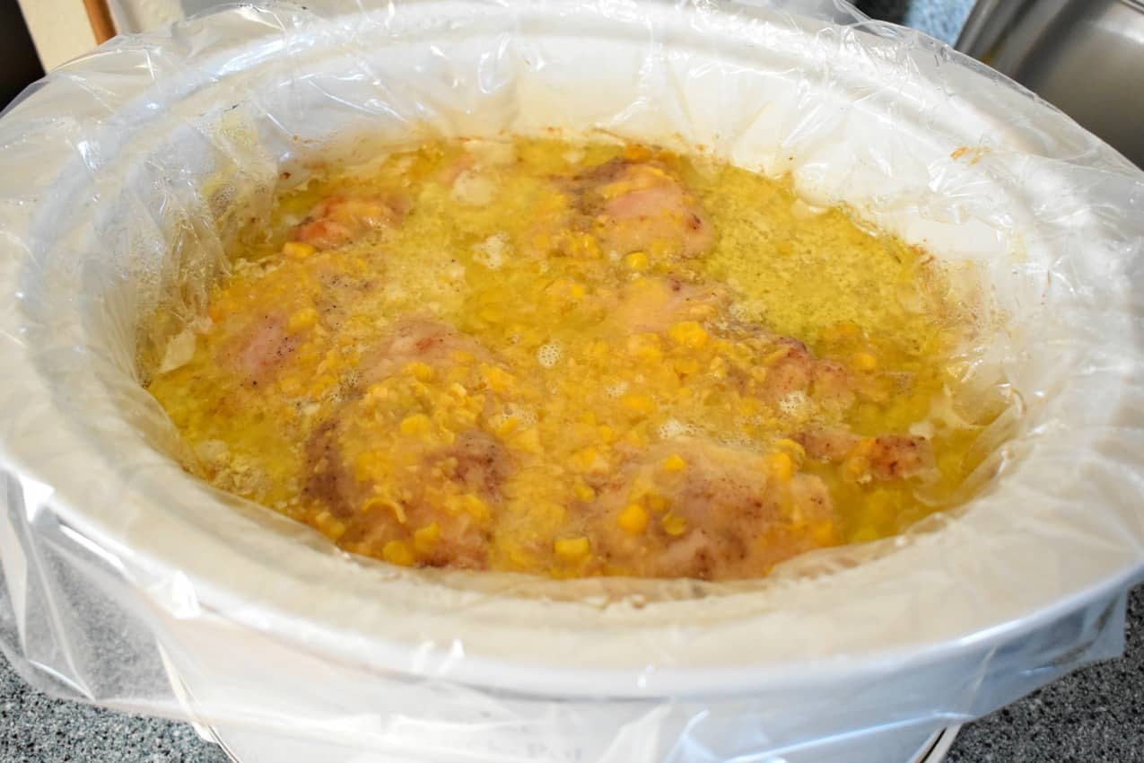 White slow cooker with a slow cooker liner filled with slow cooker chicken and corn chowder.
