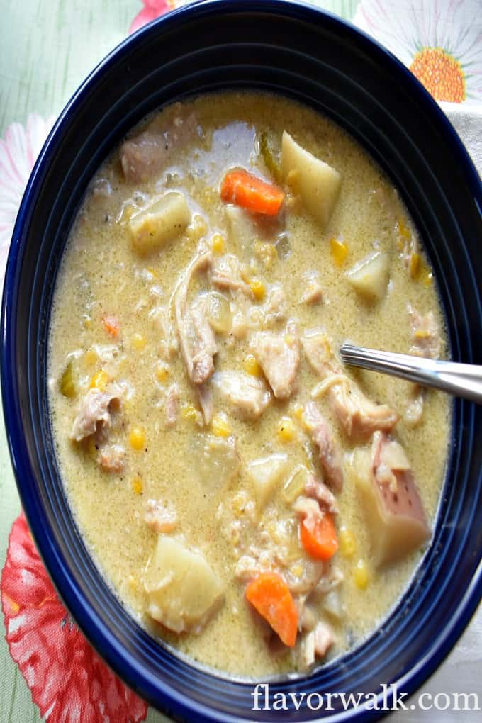 A blue bowl filled with slow cooker chicken and corn chowder and a spoon.