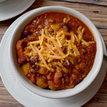 Chili with Beef, Turkey and Potatoes topped with melted cheddar cheese in white bowl sitting on round white plate | Flavor Walk
