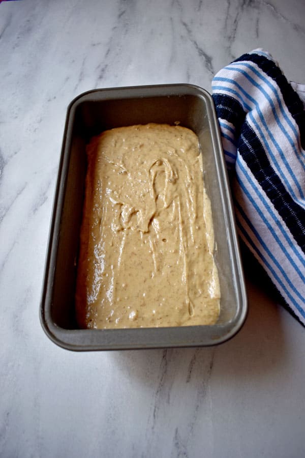 Batter for Caramelized Banana Bread {Gluten Free} in loaf pan on granite counter top with blue and white striped kitchen towel to the right of pan | Flavor Walk