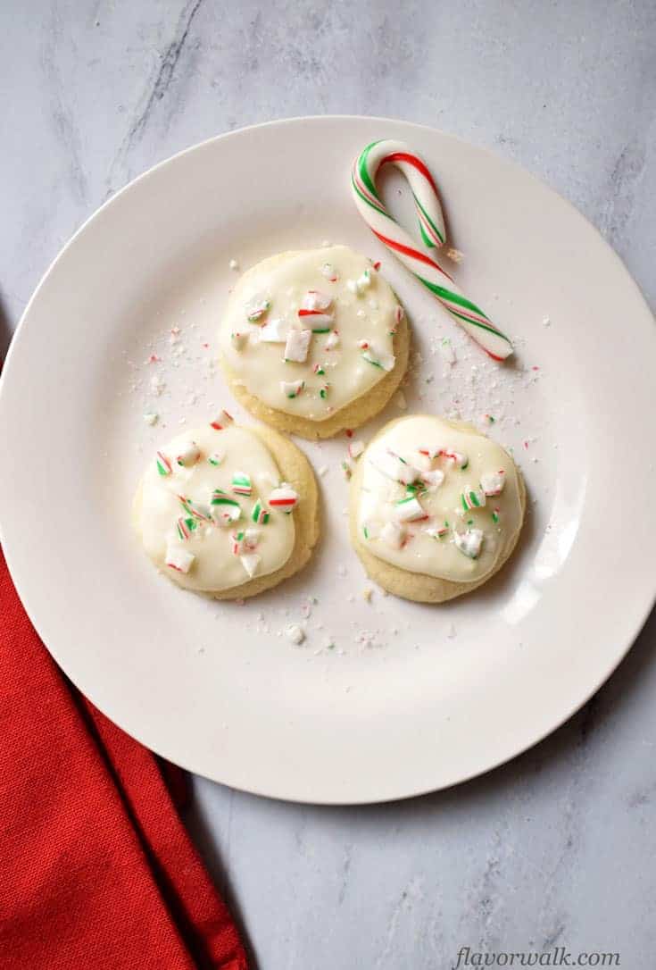 Three Gluten Free Peppermint Meltaway Cookies and a mini candy cane on white plate with red kitchen towel in the bottom left corner. | Flavor Walk