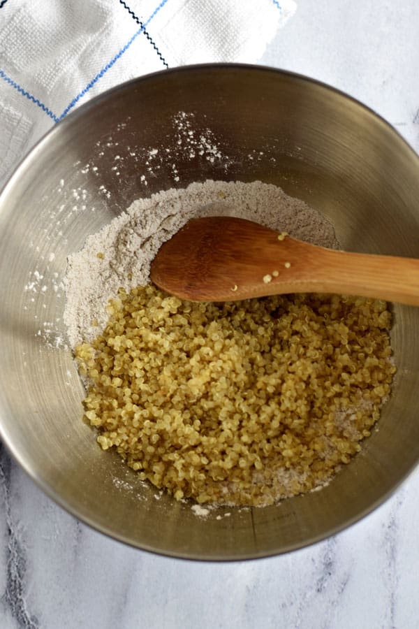 Gluten free flour mixture and cooked quinoa with wooden spoon in mixing bowl