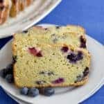 Three slices of Lemon Blueberry Bread with fresh blueberries on a white plate with more slices in the background