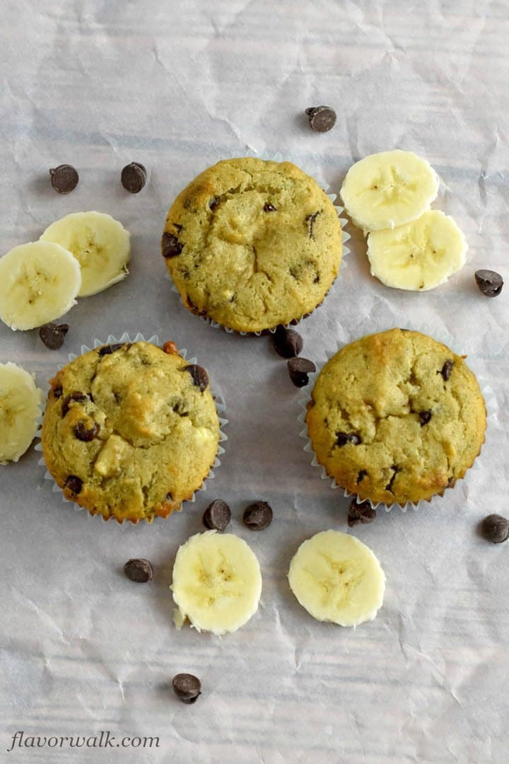 Three Gluten Free Chocolate Chip Banana Muffins on parchment paper with scattered banana slices and chocolate chips