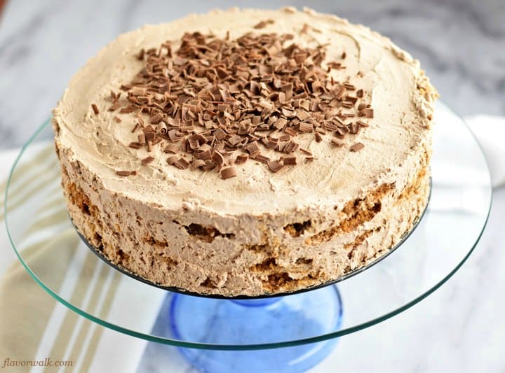 Old-Fashioned Chocolate Icebox Cake on glass cake stand with tan and white kitchen towel on the left