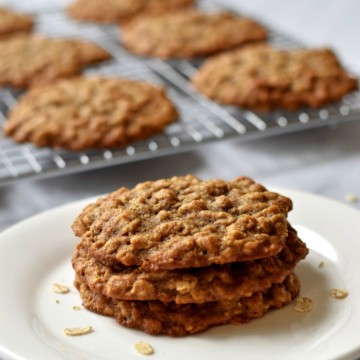 Stack of 3 banana oatmeal cookies on a white plate with additional cookies on a wire rack in the background