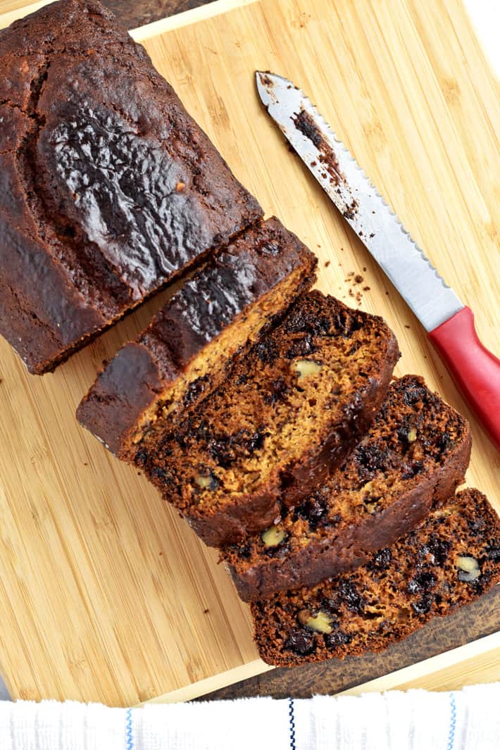 Overhead view of slices of Gluten Free Chocolate Chip and Walnut Banana Bread on a cutting board with a bread knife on the right