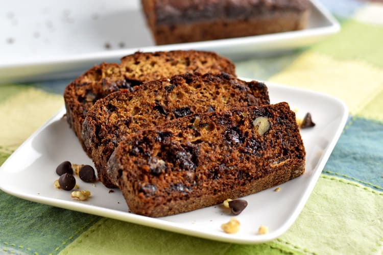 Three slices of Gluten Free Chocolate Chip and Walnut Banana Bread on small white plate with remaining loaf of bread in background