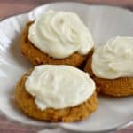 3 cream cheese frosted gluten free pumpkin cookies on silver-rimmed white plate