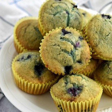 Stack of easy gluten free blueberry muffins on white plate with white striped kitchen towel in background