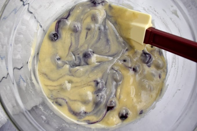 Overhead view of gluten free blueberry muffins batter with rubber spatula in glass mixing bowl