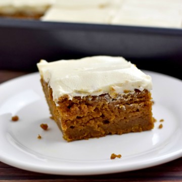 One gluten free pumpkin bar on white plate with pan of additional bars in background.