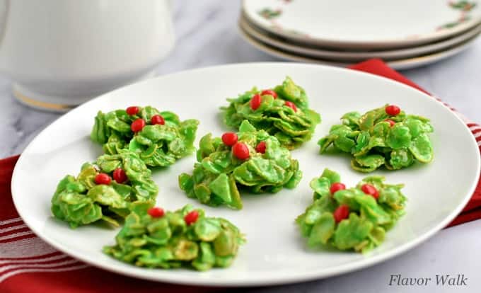 A round white plate filled with Holly Cookies on top of a red and white kitchen towel