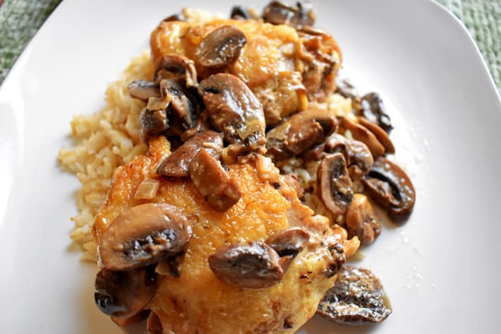 Close up shot of chicken marsala with rice on a white dinner plate