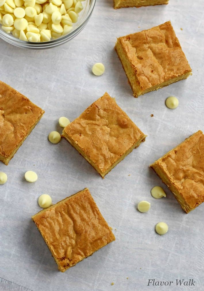 Overhead view of Gluten Free Blondies and white chocolate chips scattered on a piece of parchment paper.