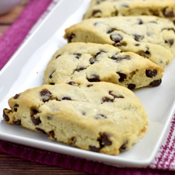 4 baked Gluten Free Chocolate Chip Scones on white rectangular plate with white coffee cup in background