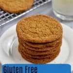 Stack of gluten free ginger snaps on small white plate with glass of milk and more cookies on wire rack in the background with blue text overlay near the bottom
