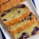 Overhead view of gluten free banana blueberry bread on white rectangular plate with blue kitchen towel under plate.