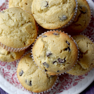 Overhead view of a stack of gluten free chocolate chip muffins on round plate sitting on purple kitchen towel.