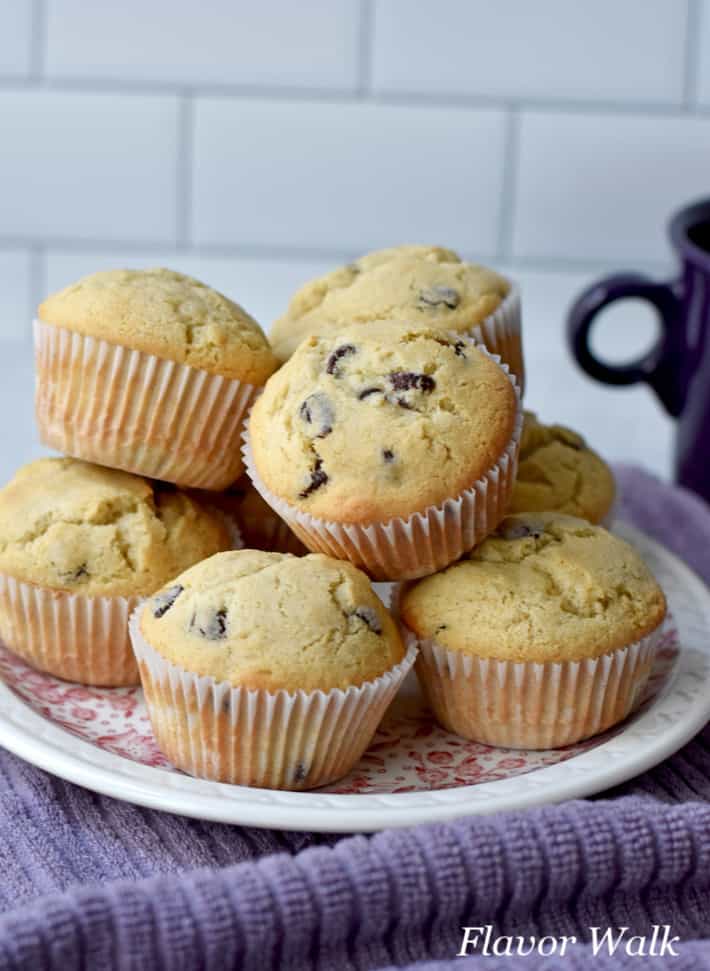 Stack of gluten free chocolate chip muffins on round plate sitting on purple kitchen towel with purple coffee cup in the background