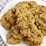 Overhead view of gluten free oatmeal raisin cookies on round white plate with purple and white striped kitchen towel underneath.
