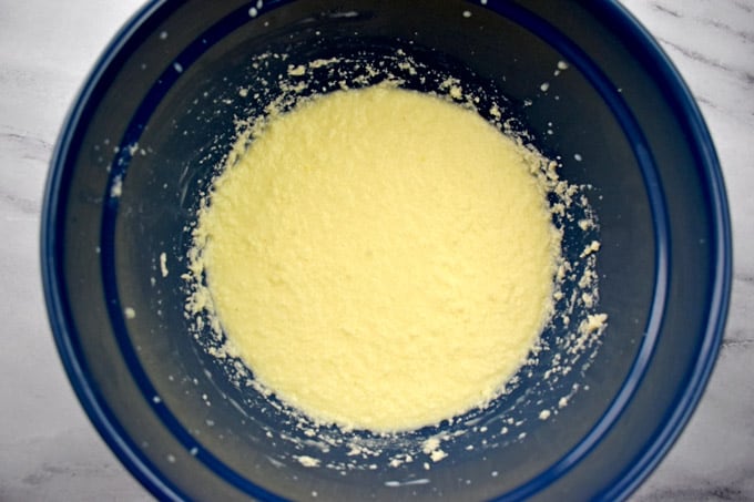 Overhead view of blue mixing bowl with butter, sugar, egg, milk, sour cream and almond extract mixed together.