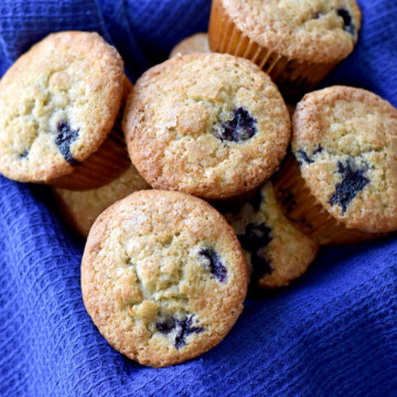 A basket, lined with a blue kitchen towel, filled with gluten free banana blueberry muffins.