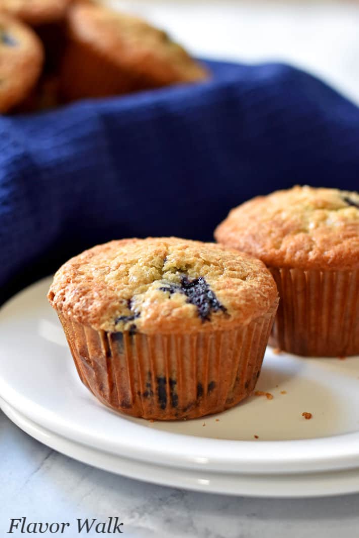 2 gluten free banana blueberry muffins on a stack of white plates with additional muffins in the background.