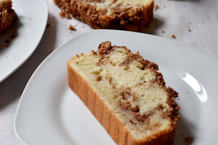 A slice of gluten free cinnamon bread on a white plate with more slices in the background.
