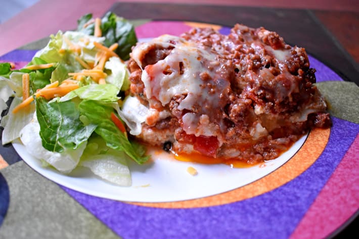 A slice of easy gluten free lasagna and a side salad on a dinner plate with an orange, purple, pink, and green design around the edge of the plate.