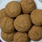 Overhead view of a stack of gluten free molasses cookies on a white plate with a rose colored kitchen towel in the bottom left corner.