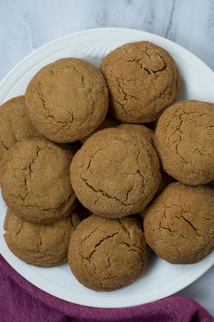 Overhead view of a stack of gluten free molasses cookies on a white plate with a rose colored kitchen towel in the bottom left corner.