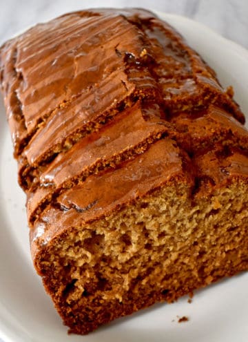 Close up view of a sliced loaf of caramelized banana bread on a white oval serving plate.