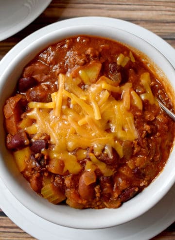 Overhead view of a white bowl filled with a serving of chili with potatoes and a fork sitting on a round white plate.