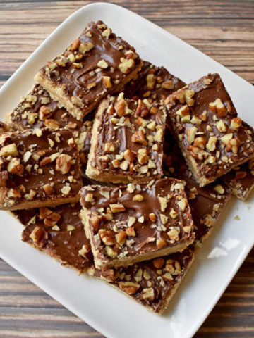 Overhead view of chocolate toffee bars stacked on a square white plate.
