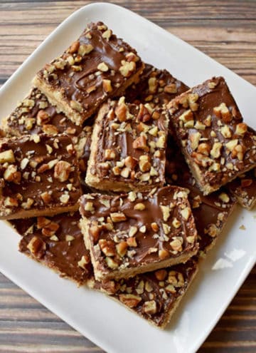 Overhead view of chocolate toffee bars stacked on a square white plate.