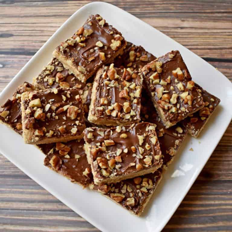 Overhead view of chocolate toffee bars stacked on a square white plate.