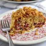A slice of cranberry coffee cake and a fork on a pink and white floral plate