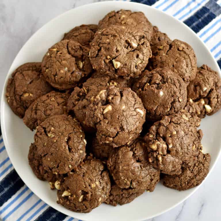 Overhead view of a white plate filled with chocolate chip pecan cookies sitting on a blue and white striped kitchen towel.