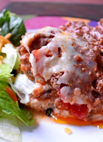 A serving of easy gluten free lasagna and a side salad on a round dinner plate.