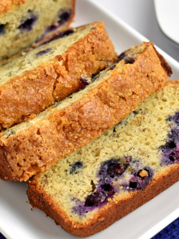 Slices of gluten free banana blueberry bread on a white rectangular plate placed on a blue kitchen towel.