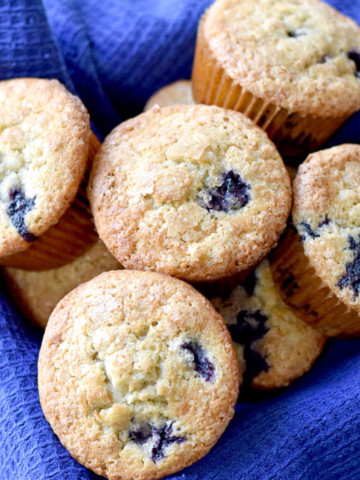 A square basket, lined with a blue towel, filled with gluten free banana blueberry muffins.