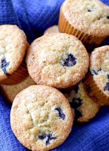 A square basket, lined with a blue towel, filled with gluten free banana blueberry muffins.
