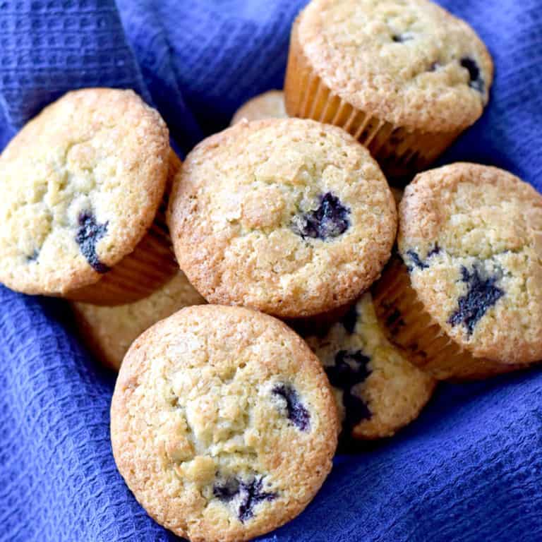 A square basket, lined with a blue towel, filled with gluten free banana blueberry muffins.