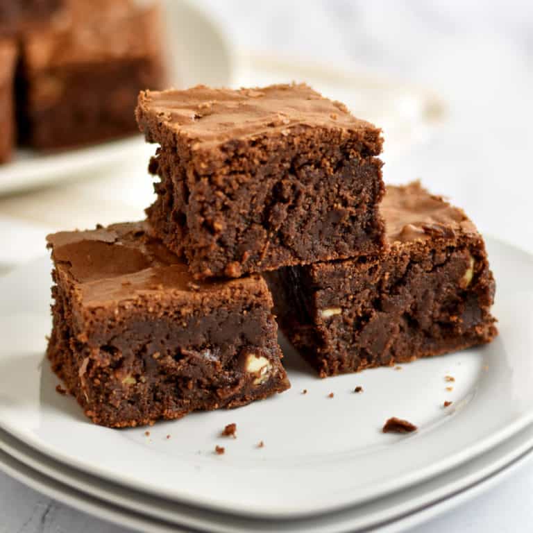 One gluten free chocolate brownie sitting on top of two more brownies on a stack of small white plates.