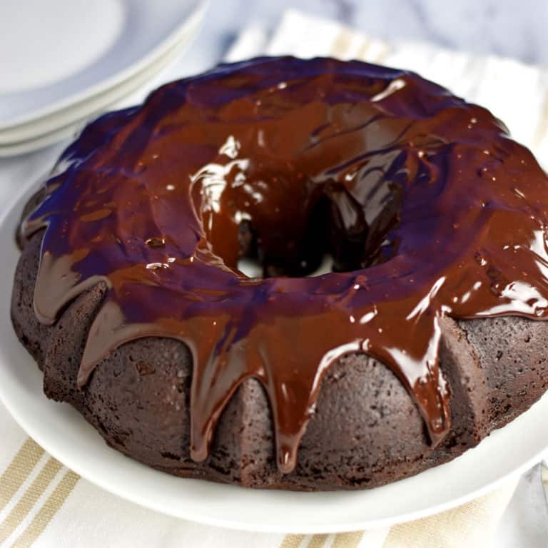 Gluten Free Chocolate Sour Cream Bundt Cake on a round white plate with a tan and white striped kitchen towel under the plate.