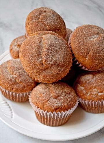 A stack of gluten free cinnamon banana muffins on a round white plate placed on a granite countertop.